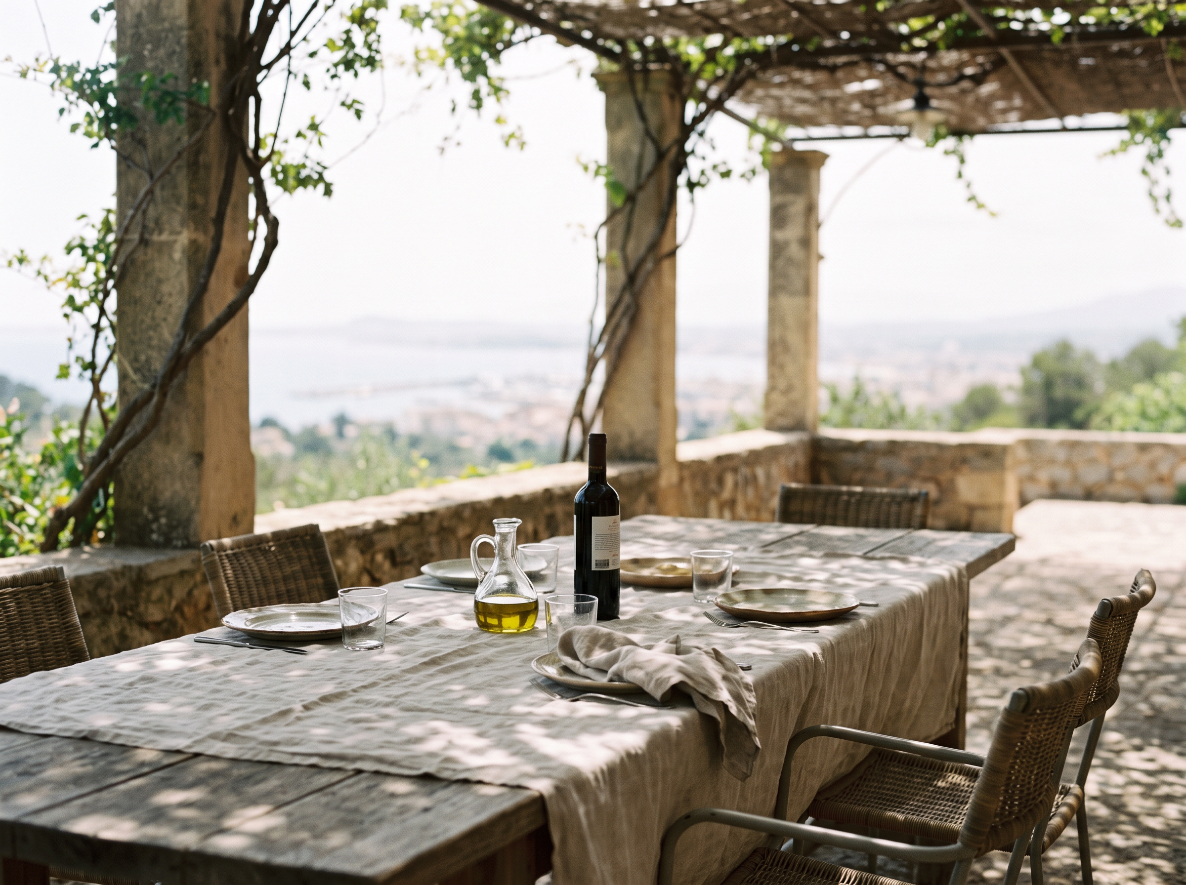 A linen-covered table set for a Mediterranean lunch in dappled shade